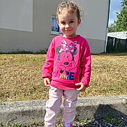 Lyana a rejoint le concours — aidez-le/la à gagner de superbes lots ! child, girl, smile, pink_sweatshirt, minnie_mouse, outdoor, sunny, grass, building, window, curb, shoes, casual_clothing, happy, young, person, daylight, fashion, cute, standing