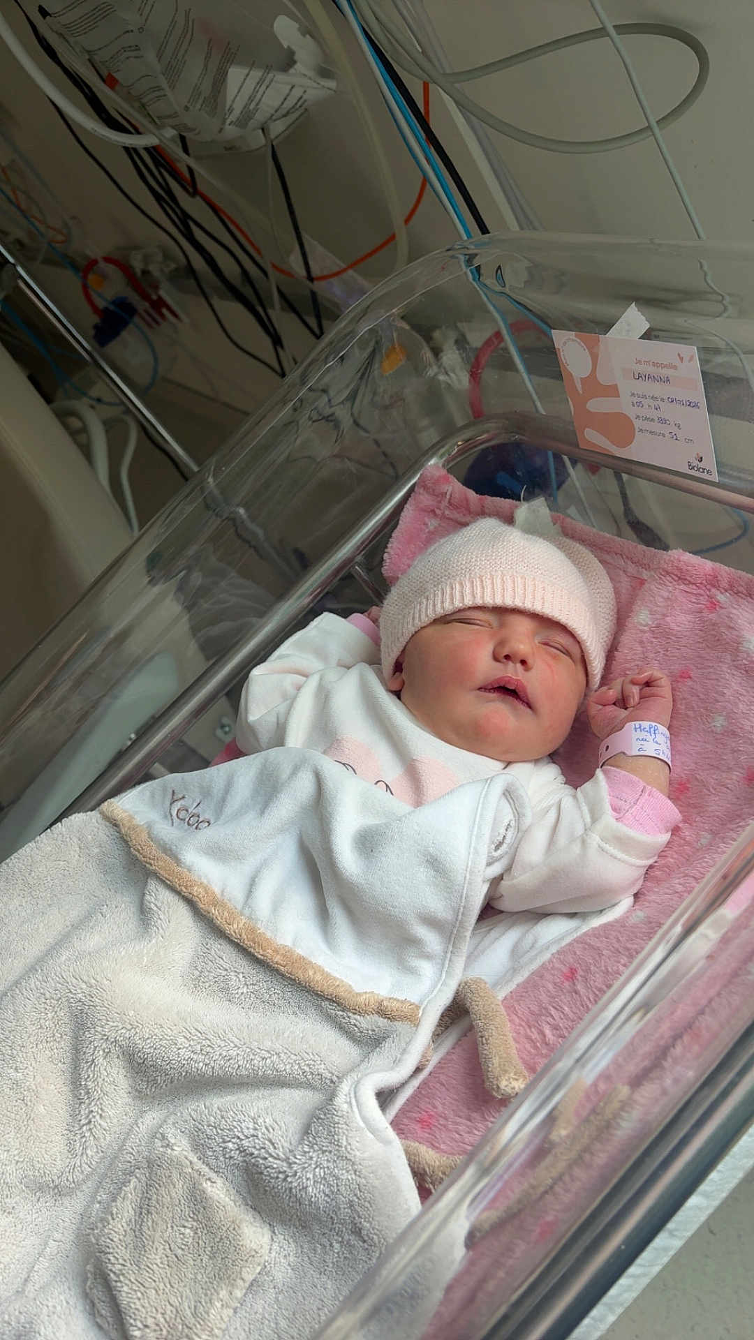 Layanna a rejoint le concours — aidez-le/la à gagner de superbes lots ! newborn, baby, hospital, bassinet, blanket, pink_hat, sleeping, medical_equipment, cozy, infant, person, resting, cute, soft, indoors, child, healthcare, wrapped, bed, peaceful