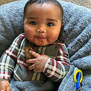 Abel joined the competition — help win amazing prizes! baby, child, face, smile, cookie, hand, blanket, plaid_clothing, cozy, indoor, carpet, happy, cute, portrait, infant, warm, toy, blue, fuzzy, snack