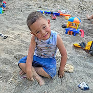 Luka is registered to the contest to win money with this photo: child, boy, sand, outdoor, play, toys, smile, happy, barefoot, shorts, tank_top, dirt, playground, summer, fun, casual_clothing, sitting, messy, daylight, nature