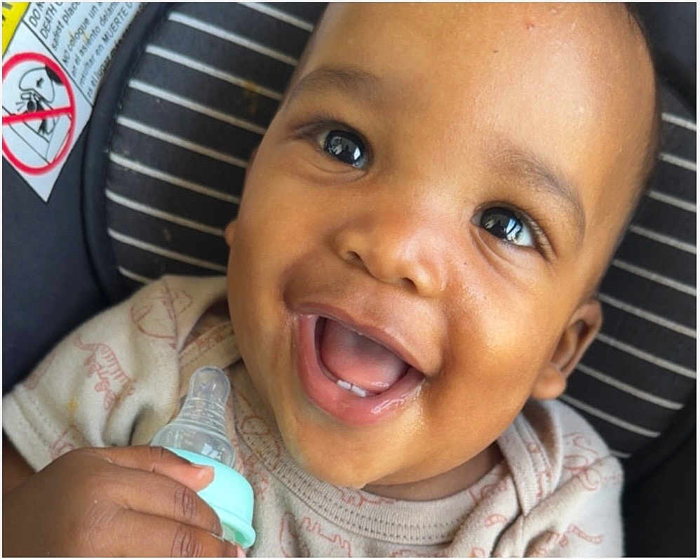 Nasir joined the competition — help win amazing prizes! baby, bottle, child, smiling, happy, face, infant, cute, teeth, hand, clothing, seat, striped, skin, mouth, portrait, closeup, young, holding, expression