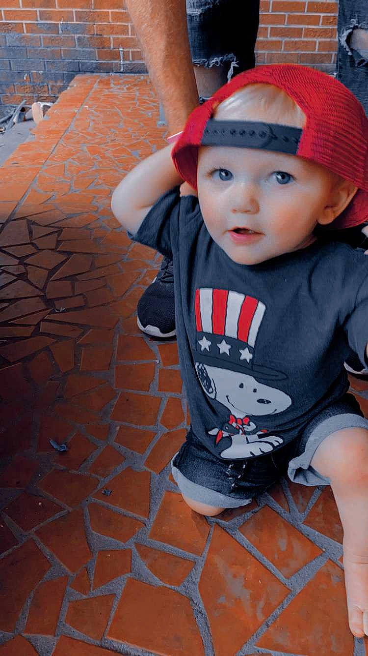 Colton is registered to the contest to win money with this photo: baby, baseball_cap, beanie, cap, carmine, child, cool, fashion_accessory, flooring, fun, grass, happy, headwear, lip, pattern, person, plant, sitting, sleeve, t_shirt