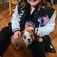 Mazie joined the competition — help win amazing prizes! girl, child, puppy, dog, bulldog, smiling, sitting, floor, wooden_floor, indoor, casual_clothing, black_pants, jacket, long_hair, cute, pet, home, furniture, blanket, happy
