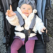 Luna a rejoint le concours — aidez-le/la à gagner de superbes lots ! baby, child, stroller, jacket, hat, smile, happy, outdoor, footwear, tights, person, clothing, seated, baby_shoes, cold_weather, playful, infant, cute, expression, transport