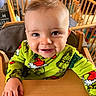Malo participe au concours pour gagner de l'argent avec cette photo : baby, child, smiling, face, high_chair, grinch, pajamas, green_clothing, indoor, furniture, wooden, infant, cute, happy, portrait, person, table, hand, room, tooth