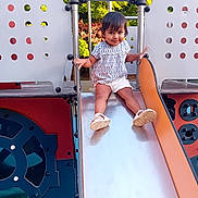 Sofia a rejoint le concours — aidez-le/la à gagner de superbes lots ! toddler, child, slide, playground, play_equipment, outdoor, smiling, shorts, shoes, metal, trees, daylight, fun, summer, person, clothing, park, happy, cute, playing