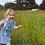 child, toddler, smiling, running, outdoor, grass, wildflowers, blue_dress, boots, nature, trees, meadow, greenery, happy, sky, cloudy, field, cute, playful, person