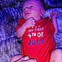 baby, newborn, infant, onesie, red_clothing, hand, blanket, soft_texture, purple_lighting, lying_down, person, toddler, small_hands, cute, celebration, festive, sleepy, skin, face, portrait