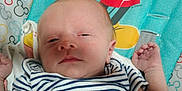Kolten is registered to the contest to win money with this photo: baby, infant, striped_clothing, mickey_mouse, blanket, cartoon, sleepy, lying_down, child, cute, toddler, face, head, arm, hand, pattern, colorful, smiling, portrait, indoors