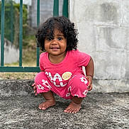 Djune participe au concours pour gagner de l'argent avec cette photo : toddler, child, curly_hair, pink_clothing, squatting, barefoot, outdoor, concrete, fence, wall, happy, smiling, person, casual, flower_pattern, lemon_graphic, daylight, portrait, cute, young_child