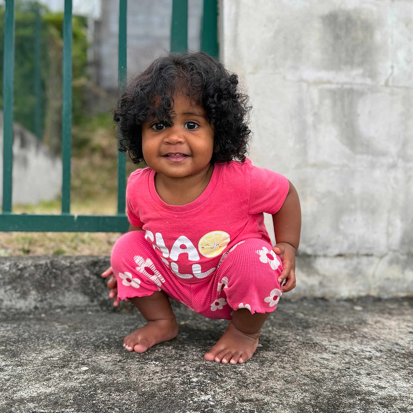 Djune participe au concours pour gagner de l'argent avec cette photo : toddler, child, curly_hair, pink_clothing, squatting, barefoot, outdoor, concrete, fence, wall, happy, smiling, person, casual, flower_pattern, lemon_graphic, daylight, portrait, cute, young_child