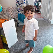 Sullivan is registered to the contest to win money with this photo: balloon, box, boy, child, clothing, dress, face, furniture, head, indoors, interiordesign, male, pants, person, photography, portrait, shorts, standing, t_shirt, wood