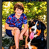 Bryler is registered to the contest to win money with this photo: animal, bernese_mountain_dog, boy, casual_clothing, child, dog, friendship, greenery, happy, leaf_litter, nature, outdoor, pet, portrait, rock, shorts, sitting, smiling, sneakers, sunlight