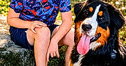 Bryler is registered to the contest to win money with this photo: child, boy, dog, bernese_mountain_dog, outdoor, smiling, nature, greenery, sunlight, happy, sitting, pet, animal, casual_clothing, shorts, sneakers, necklace, grass, leaves, portrait
