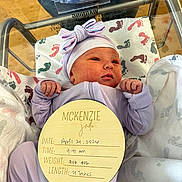 Mckenzie is registered to the contest to win money with this photo: newborn, baby, hospital, bassinet, blanket, footprints, hat, bow, purple_clothing, infant, cute, sleeping, sign, name_tag, baby_girl, portrait, child, hospital_room, wrapped, resting