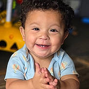 Lincoln is registered to the contest to win money with this photo: child, toddler, smile, clapping, curly_hair, blue_clothing, onesie, hot_air_balloon_pattern, happy, indoors, wooden_floor, face, baby, cute, hands, person, infant, portrait, sitting, playful