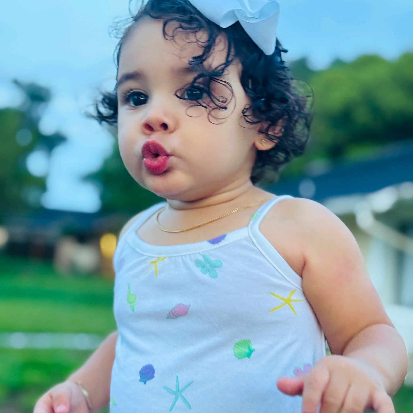 Ainhoa is registered to the contest to win money with this photo: blue_sky, bow, bracelet, child, curly_hair, cute, daylight, dress, expression, funny_face, gold_necklace, green_background, jewelry, nature, outdoor, person, portrait, sea_shell_pattern, summer, toddler