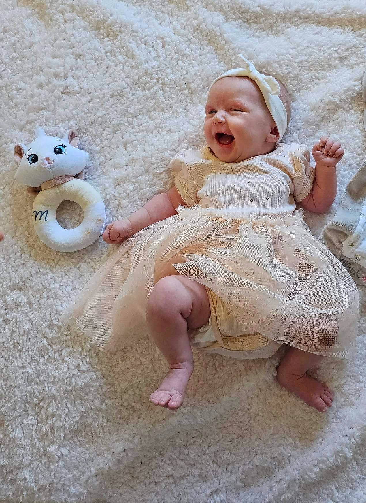 Tessa a rejoint le concours — aidez-le/la à gagner de superbes lots ! baby, baby_toddler_clothing, comfort, dress, fawn, foot, fun, fur, happy, head, human_body, iris, person, pink, sitting, skin, sleeve, smile, toddler, toy