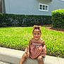 child, toddler, smiling, dress, headband, sandals, grass, curb, outdoor, sunlight, hedge, happy, sitting, person, nature, footwear, accessory, greenery, daytime, casual