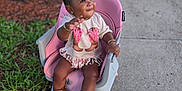 E'Nyla is registered to the contest to win money with this photo: toddler, child, pink_chair, boots, sidewalk, grass, tree, outdoor, smiling, waving, jewelry, bracelets, necklace, fringed_shirt, brown_boots, short_hair, happy, person, daylight, cute