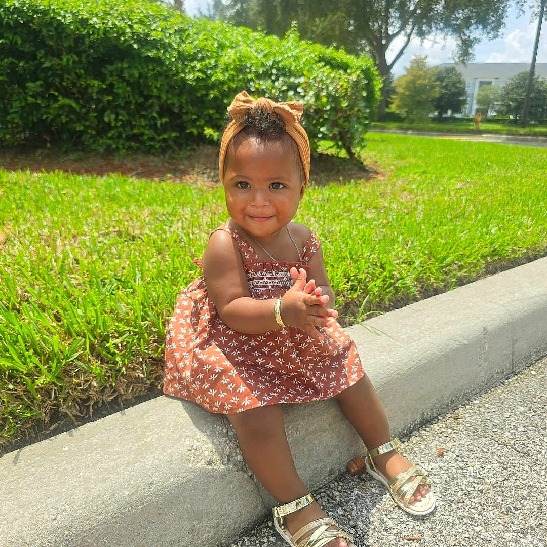 E'Nyla is registered to the contest to win money with this photo: casual, child, curb, daytime, dress, grass, greenery, happy, headband, nature, outdoor, person, playful, sandals, sidewalk, smiling, sunny, toddler, tree, young_child