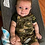 Weston is registered to the contest to win money with this photo: baby, child, camo_overalls, smile, drool, blanket, chair, cushion, face, skin, arm, hand, legs, indoor, wood_floor, clothing, comfort, cute, portrait, young