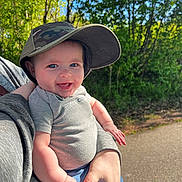 Weston joined the competition — help win amazing prizes! baby, child, smiling, cap, camo, outdoor, nature, trees, sunlight, person, holding, happy, face, blue_eyes, shirt, short_sleeve, jeans, hand, adult, path