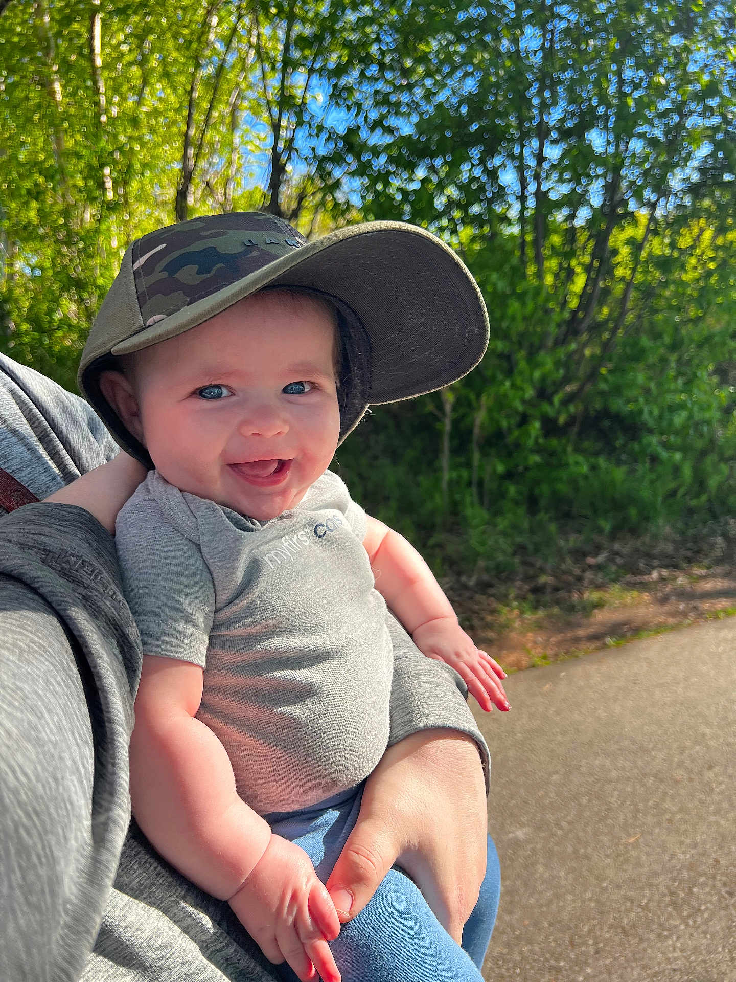 Weston joined the competition — help win amazing prizes! baby, child, smiling, cap, camo, outdoor, nature, trees, sunlight, person, holding, happy, face, blue_eyes, shirt, short_sleeve, jeans, hand, adult, path