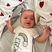 Aaron participe au concours pour gagner de l'argent avec cette photo : arm, baby, bed, blanket, cartoon, child, cute, face, happy, hearts, infant, lying_down, onesie, pattern, person, red, sleepwear, smiling, soft, white