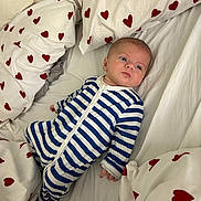 Aaron participe au concours pour gagner de l'argent avec cette photo : baby, infant, bed, bedding, pillow, onesie, striped_clothing, heart_pattern, fabric, sleepwear, child, person, indoor, resting, cute, young_child, comfort, soft, lying_down, blue