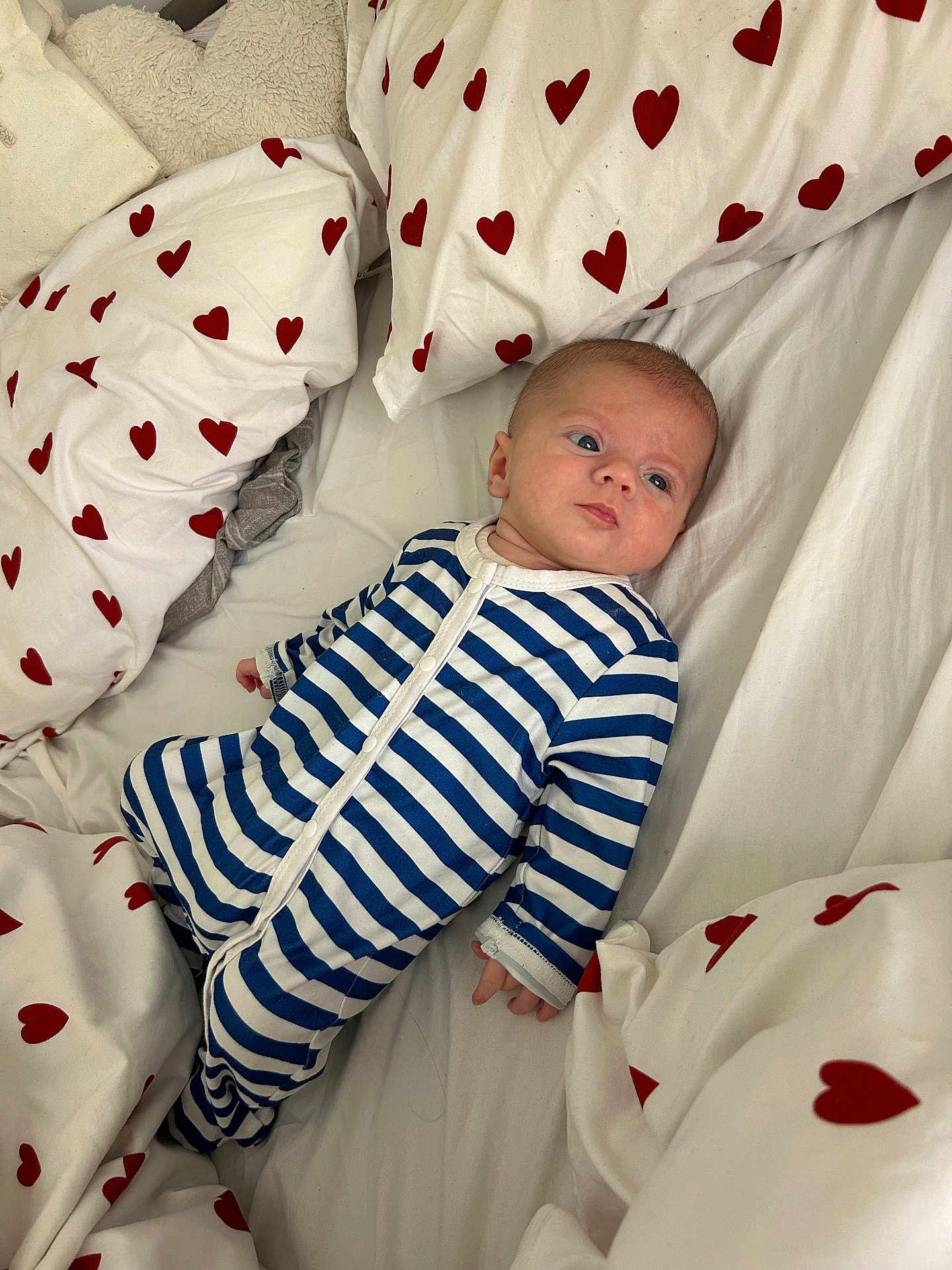 Aaron participe au concours pour gagner de l'argent avec cette photo : baby, infant, bed, bedding, pillow, onesie, striped_clothing, heart_pattern, fabric, sleepwear, child, person, indoor, resting, cute, young_child, comfort, soft, lying_down, blue
