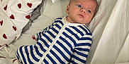Aaron participe au concours pour gagner de l'argent avec cette photo : baby, infant, bed, bedding, pillow, onesie, striped_clothing, heart_pattern, fabric, sleepwear, child, person, indoor, resting, cute, young_child, comfort, soft, lying_down, blue