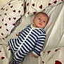 baby, infant, bed, bedding, pillow, onesie, striped_clothing, heart_pattern, fabric, sleepwear, child, person, indoor, resting, cute, young_child, comfort, soft, lying_down, blue