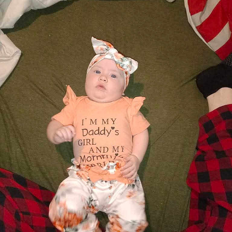 Peyton is registered to the contest to win money with this photo: baby, black, blanket, casual, child, clothing, cute, floral_pattern, green, headband, indoors, infant, lying_down, pants, person, plaid, portrait, red, shirt, soft_fabric