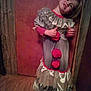 blurry, child, clown_costume, costume, dim_light, door, dressed_up, expression, floor, head_tilt, indoor, person, playful, pom_poms, portrait, standing, vintage_clothing, wooden_door, wooden_floor, young_child
