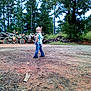 casual_clothing, child, daylight, dirt, environment, footwear, forest, grass, jeans, logs, nature, outdoor, person, playful, pose, smile, trees, tshirt, wood, young