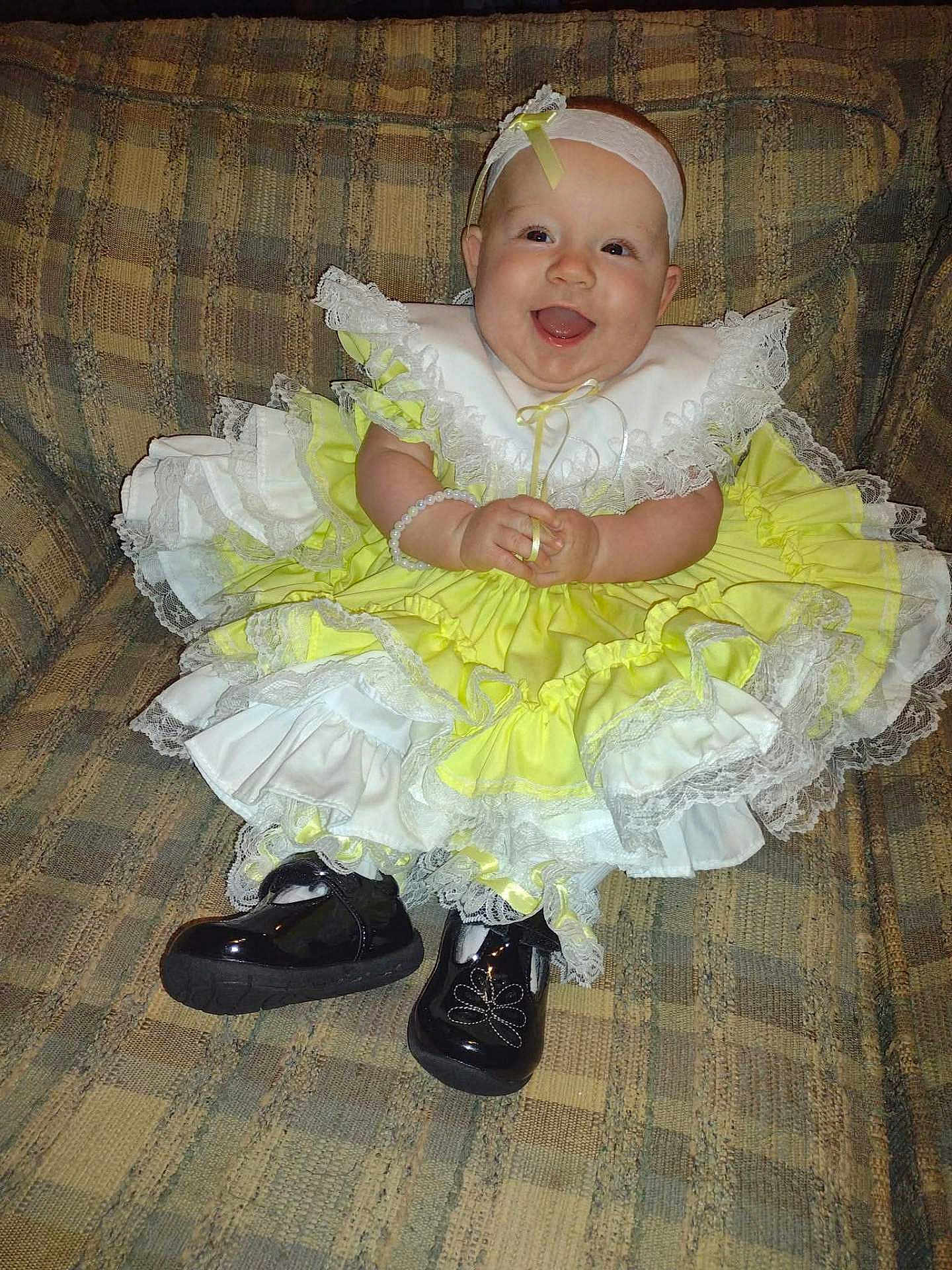 Layla is registered to the contest to win money with this photo: baby, child, smile, dress, yellow, white, lace, headband, shoes, black_shoes, couch, sitting, happy, portrait, indoor, cute, infant, clothing, accessory, joyful
