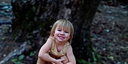 Layla is registered to the contest to win money with this photo: child, smiling, barefoot, forest, tree, nature, outdoor, happy, young, blonde_hair, sitting, woodland, person, casual, daylight, ground, tree_trunk, playful, bare_legs, cute