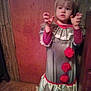 child, clown_costume, costume, curious_expression, door, floor, furniture, hands, indoor, light, long_sleeves, person, playful, pom_poms, portrait, red, room, standing, wooden_floor, young_child
