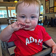 Parker is registered to the contest to win money with this photo: baby, child, infant, portrait, restaurant, high_chair, red_shirt, sitting, face, blue_eyes, brown_hair, smiling, hand, fingers, food, plastic_bag, indoor, furniture, background, photography