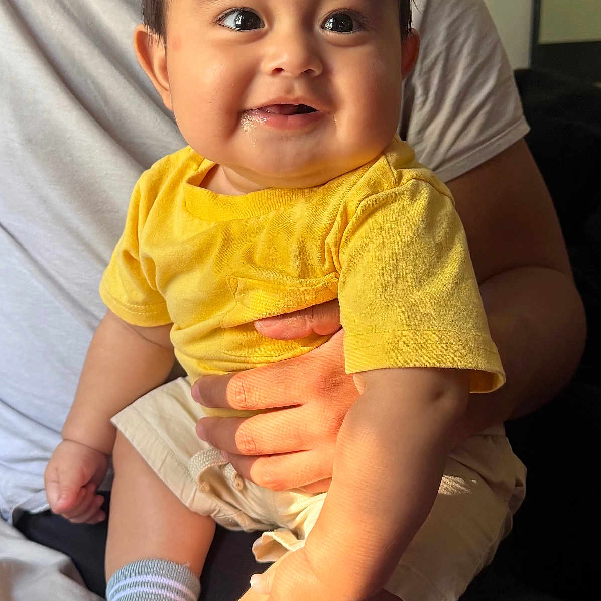 Danny joined the competition — help win amazing prizes! baby, child, infant, smiling, happy, portrait, indoor, sitting, yellow_shirt, shorts, socks, adult, parent, arms, closeup, face, eyes, family, home, photography