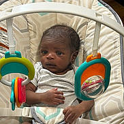 Kyaire is registered to the contest to win money with this photo: baby, baby_seat, child, clothing, colorful, cushion, cute, face, hands, human, indoor, infant, plastic_toy, playtime, seat_belt, small, striped_shirt, toy, wood_floor, young