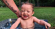 Jaxxon is registered to the contest to win money with this photo: arm, baby, child, cute, daylight, grass, happy, metal_tub, nature, outdoor, person, playful, skin, smiling, splashing, summer, tattoo, toddler, tree, water