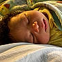 baby, sleeping, blanket, curly_hair, face, infant, cozy, soft_light, yellow_clothing, peaceful, closeup, cute, child, indoors, resting, warm_colors, portrait, toddler, comfort, nap