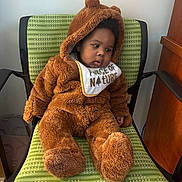 Desahn is registered to the contest to win money with this photo: baby, bear_costume, bib, brown, chair, child, clothing, costume, cozy, cute, fluffy, furniture, green_chair, indoor, looking_sideways, person, portrait, seated, toddler, young_child