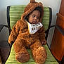 baby, bear_costume, bib, brown, chair, child, clothing, costume, cozy, cute, fluffy, furniture, green_chair, indoor, looking_sideways, person, portrait, seated, toddler, young_child