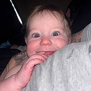 Trinity joined the competition — help win amazing prizes! baby, child, close_up, curious, cute, expression, eyes, face, fingers, hand, indoor, infant, nibble, person, playful, portrait, skin, smile, soft_lighting, tattoo