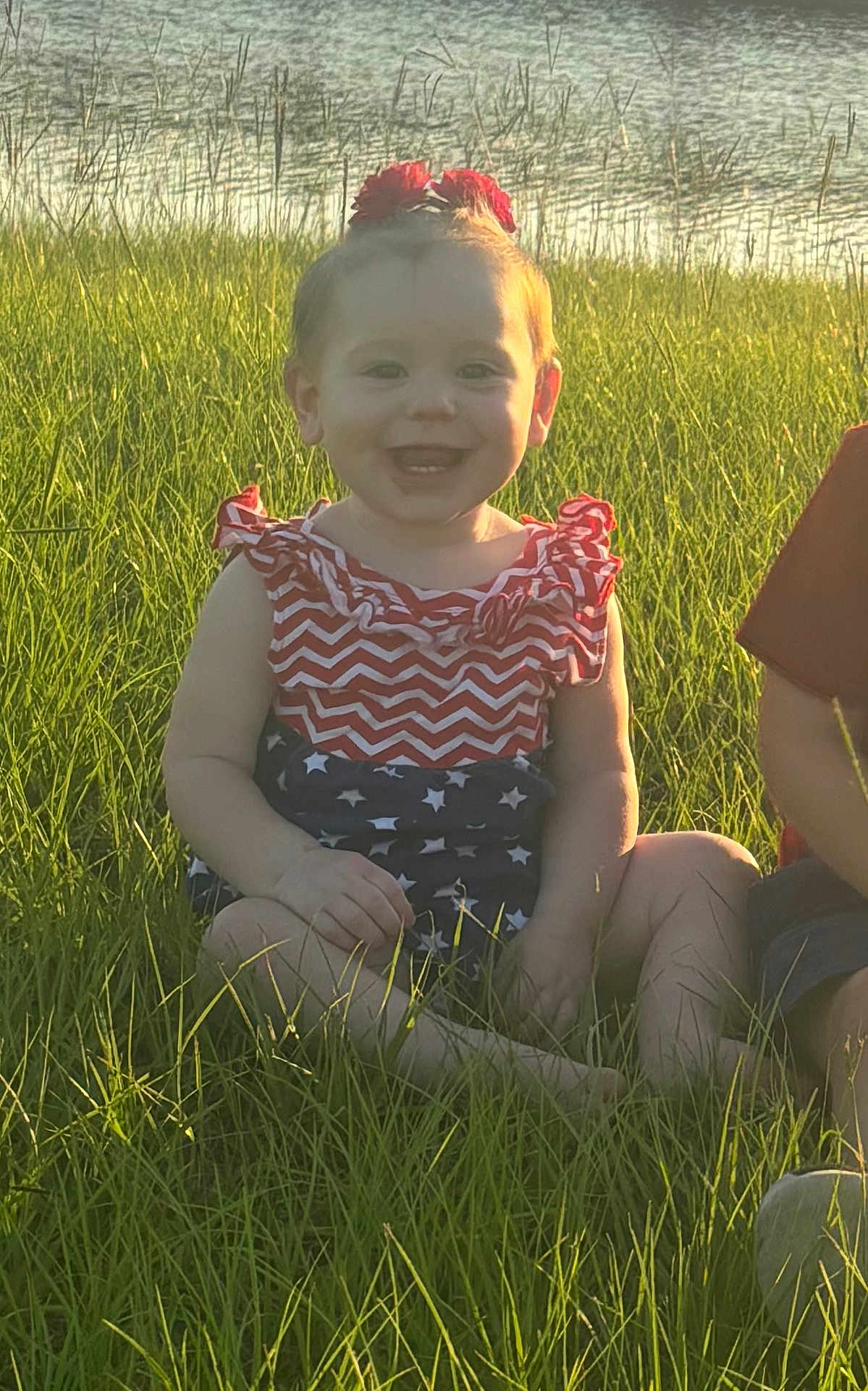 Trinity is registered to the contest to win money with this photo: baby, child, grass, outdoor, sunlight, water, field, smile, happy, sitting, headband, red, blue, white, stars, stripes, nature, summer, portrait, cute