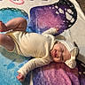 baby, infant, blanket, butterfly, headband, tongue_out, playful, indoors, carpet, toy, colorful, child, smiling, cute, lying_down, clothing, floor, person, happy, young