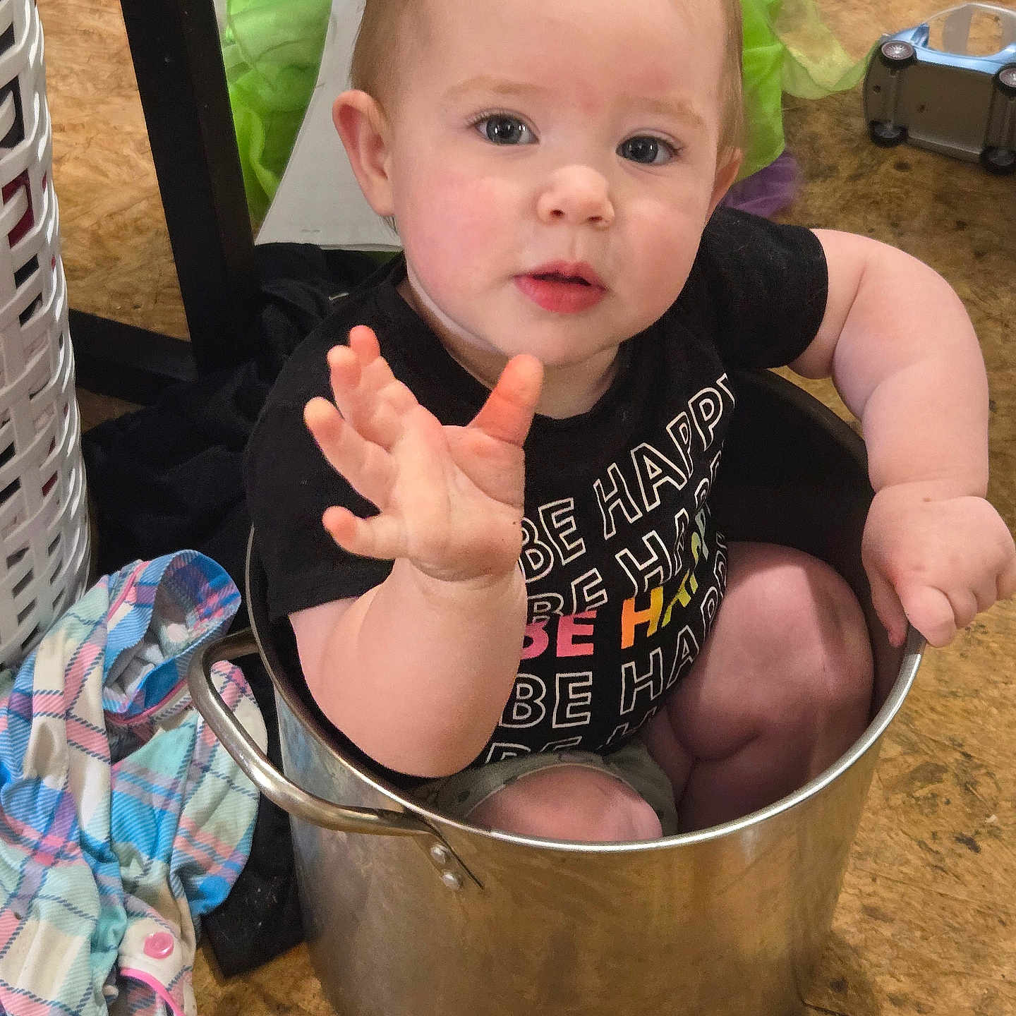 Vaseiya joined the competition — help win amazing prizes! baby, black_tshirt, child, clothing, curious, face, floor, hand, household_items, indoor, laundry_basket, metal_pot, plaid_cloth, pot, reaching_hand, sitting, text_on_clothing, toddler, toy_car, wooden_floor